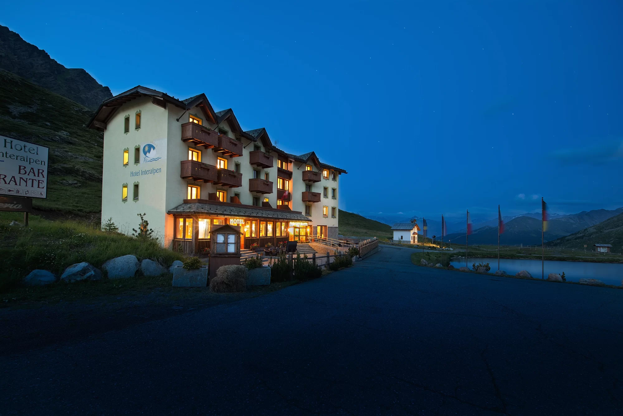 Hotel alpino illuminato di notte con montagne sullo sfondo.