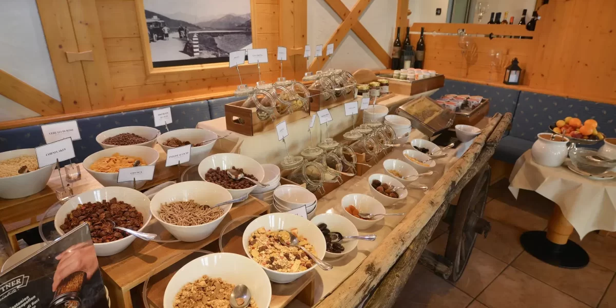 Buffet di cereali, frutta secca e ingredienti per la colazione esposto su un tavolo in legno.