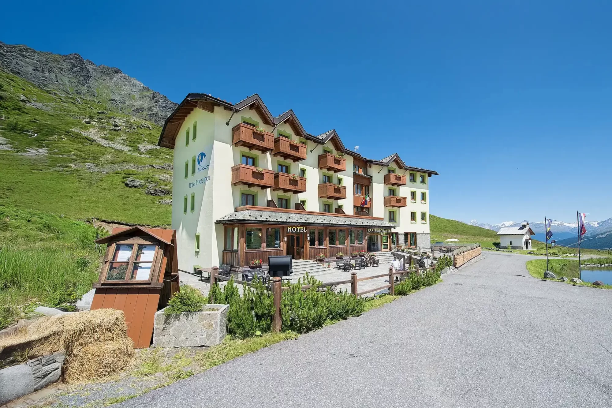 Hotel alpino con balconi in legno, situato in una valle montana con cielo blu chiaro.