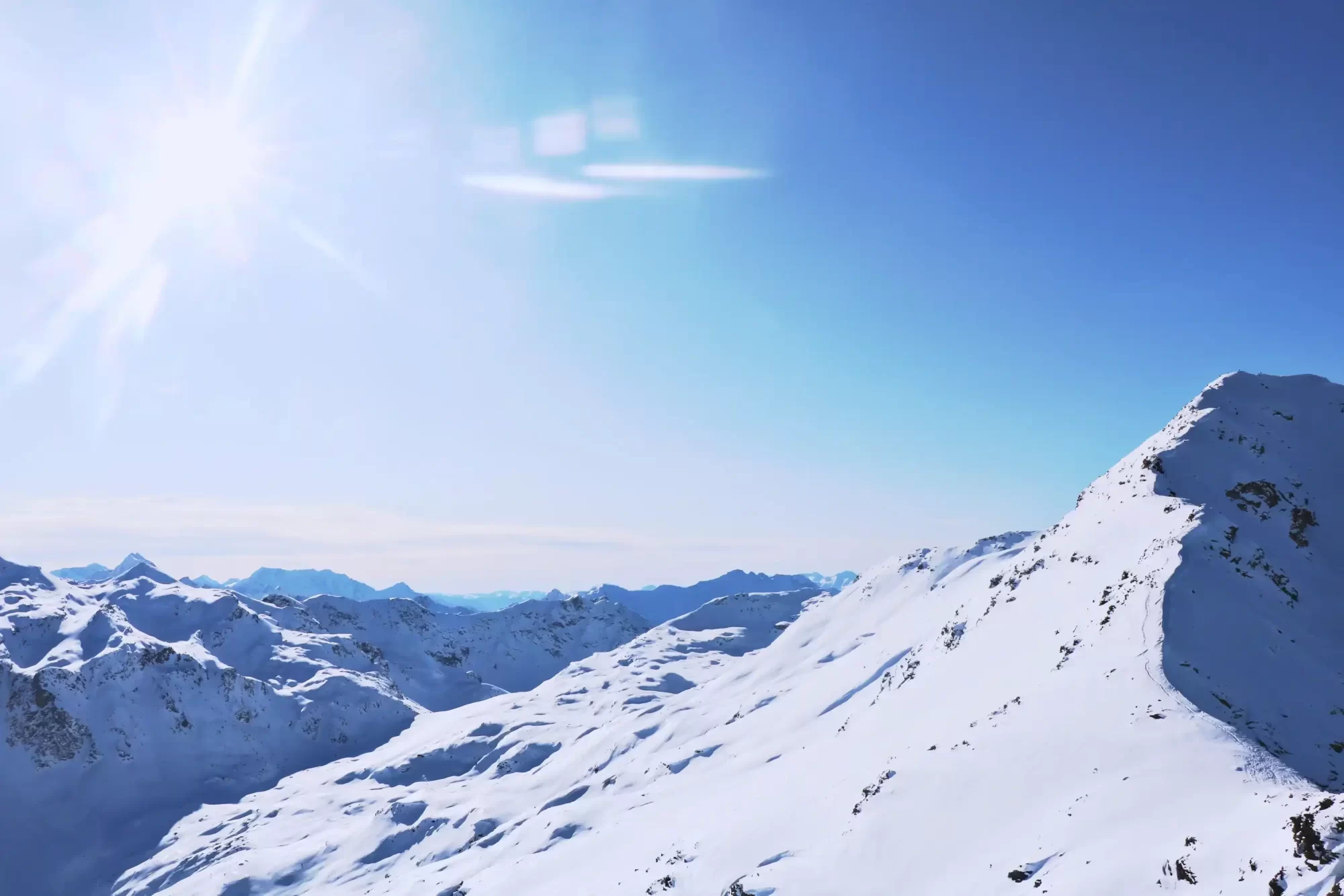 Una catena montuosa innevata illuminata dal sole in un cielo sereno.