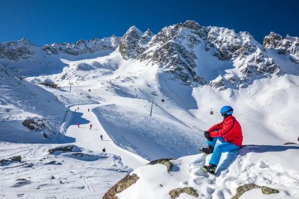 Scenico panorama alpino con sciatore che si riposa su una roccia innevata.