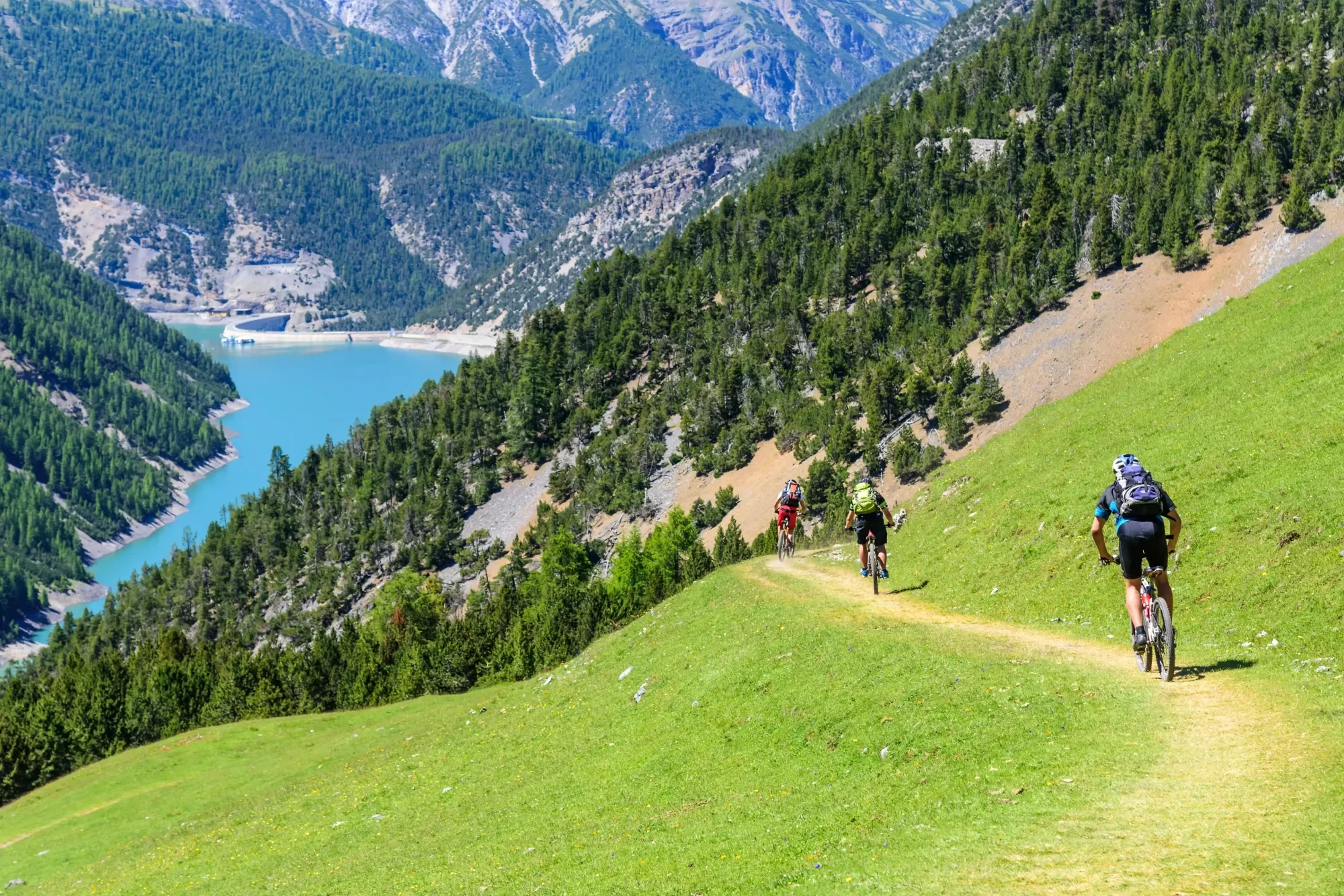 Ciclisti percorrendo un sentiero verde in montagna vicino a un lago alpino.