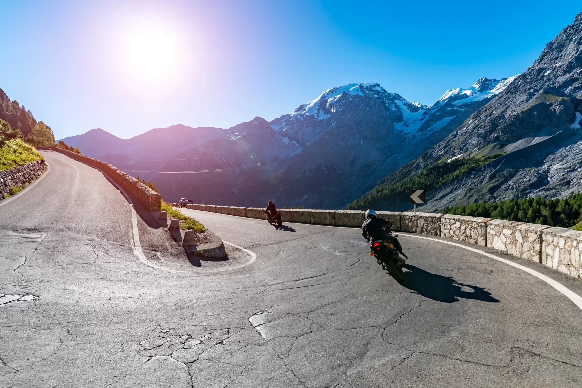 Motociclisti percorrono una strada di montagna con il sole che splende in lontananza.