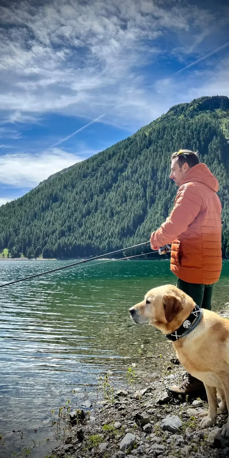 Uomo e cane vicino a un lago di montagna durante una giornata di pesca.