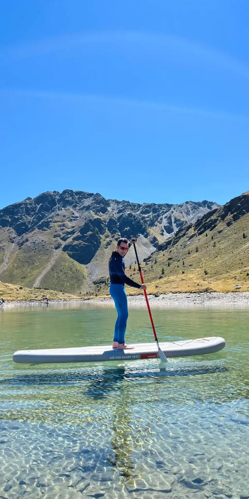 Una persona fa paddleboarding su un lago cristallino con montagne sullo sfondo.