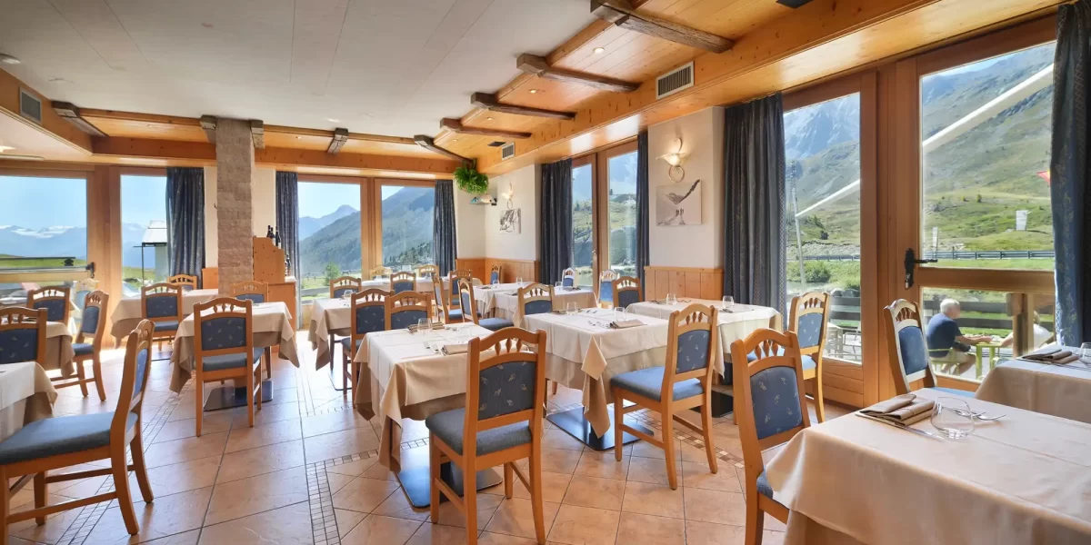 Sala da pranzo luminosa con vetrate panoramiche su un paesaggio montano.