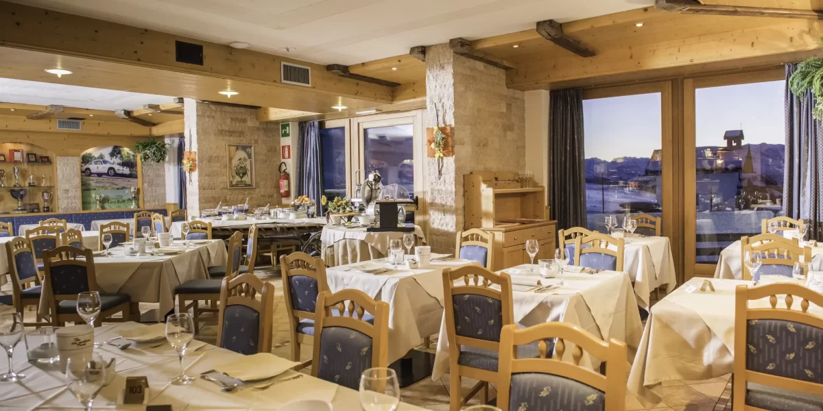 Interno di un ristorante accogliente con tavoli apparecchiati e vista panoramica sul paesaggio montano.