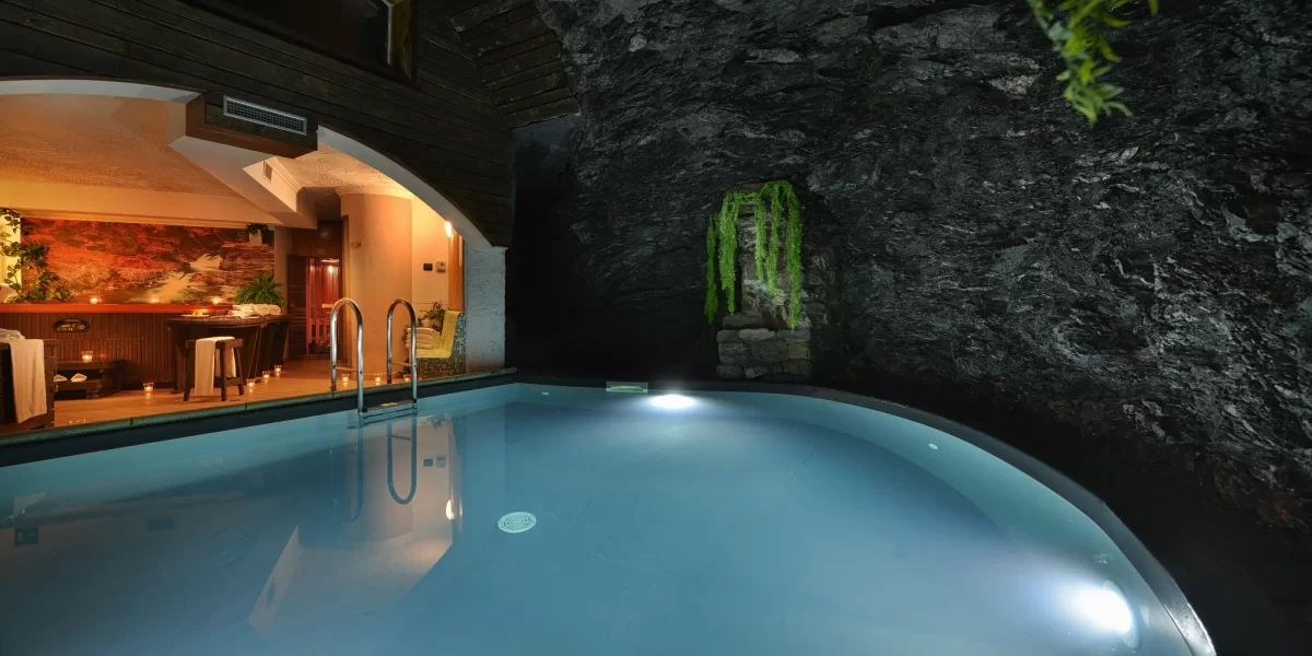 Piscina illuminata in una grotta con area relax e decorazioni naturali.